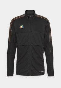 Sort zip-up jakke med farverige vandrette striber langs skuldrene, med et broderet logo på venstre bryst og mesh-paneler.