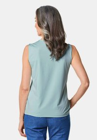 Top senza maniche in tessuto blu pallido, con una texture liscia e un collo rotondo, abbinato a jeans blu casual.