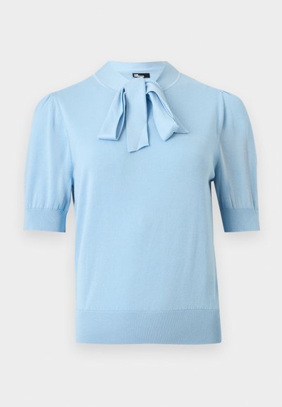 Haut tricoté bleu clair à manches courtes avec poignets et ourlet côtelés, présentant un détail de nœud noué au col rond.