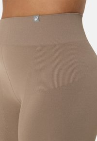 Brown high-waisted leggings with ribbed texture, featuring a logo tag and a smooth finish. Seam detailing provides a fitted look.