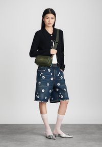 Mörk stickad cardigan, blå denimshorts med vitt blommönster, grön axelväska och silverskor med rosetter och vita strumpor.