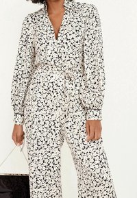 Set di blusa e pantaloni floreali in bianco e nero, con colletto, maniche lunghe e una cintura in vita. Tessuto morbido con una leggera lucentezza.