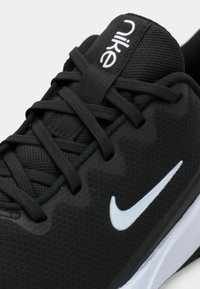 Crni Nike tenisice s teksturiranim mrežastim gornjim dijelom, ravnim vezicama i bijelim Swoosh logotipom. Imaju podstavljenu podršku za stopalo i ojačane rupice za vezice.