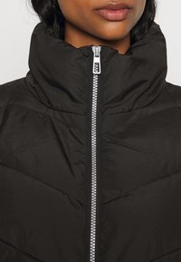 Giubbotto piumino nero con alto colletto, chiusura a zip frontale e motivo trapuntato. Presenta dettagli in metallo argentato e una texture liscia e opaca.
