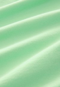 Tissu en coton vert clair avec une texture lisse et douce. Il présente des rides subtiles et une couleur uniforme sans motifs ni éléments métalliques.