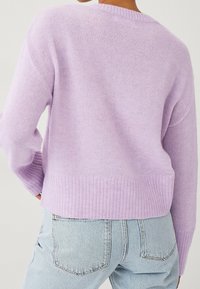 Maglione leggero lavanda con orlo e polsini a costine, caratterizzato da una vestibilità ampia e una texture morbida, abbinato a jeans azzurri.