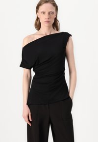 Melnas blūzes bez pleciem, kas izgatavota no mīksta auduma, ar plandošu dizainu un īsām piedurknēm, kombinēta ar brīvām melnām biksēm.