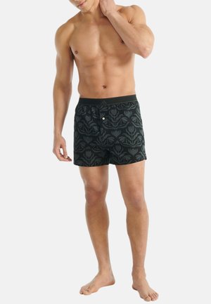 Zwarte zwemshorts met een bloemenpatroon, een elastische tailleband en een sluiting met knoop aan de voorkant, gemaakt van lichtgewicht, ademend materiaal.