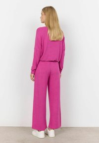 Ružový, voľne strihaný outfit s dlhými rukávmi a širokými nohavicami, vyrobený z mäkkého materiálu. Má jednoduchý dizajn a ležérny štýl.