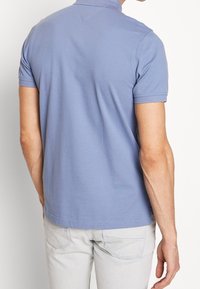 Short-sleeve polo shirt in light blue, soft cotton fabric. Features a collar and a stitched hem. Back view shows shoulder seam and minimal detailing.
