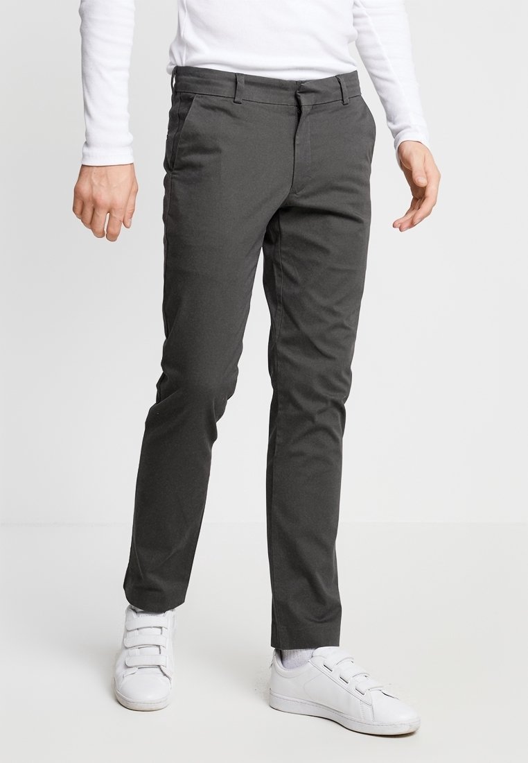 Mörkgrå chinos med slim fit, med slät front, sidofickor och bälteshällor, kombinerat med vita sneakers. Slät tygtextur.