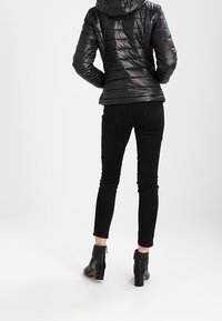 Zwarte pufferjas met een glanzende afwerking en een capuchon, gecombineerd met zwarte slim-fit jeans en zwarte enkelhoge laarzen met een blokhak.