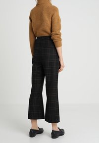 Hnědý pletený svetr s žebrovanou strukturou, kombinovaný s černo-zelenými vysokým pasem kostkovanými kalhotami. Na spodní části jsou vidět černé boty.