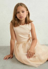 Svijetloružičasti top bez rukava u kombinaciji s slojevitom suknjom od tila do koljena, koja ima suptilne zlatne točkice i naborani pojas.