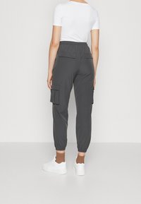 Harmaat cargo-housut rentoa leikkausta, joissa on sivutaskuja ja elastiset hihnat, yhdistettyinä valkoisiin tennareihin ja ruskeisiin nilkkasukkiin.