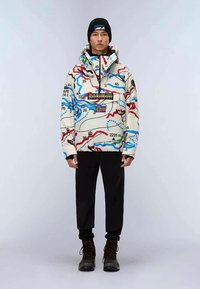 Colorful map-patterned jacket in cream with blue and red lines, featuring a zippered collar and a branded patch. Worn with black pants and boots.