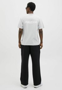 Lys grå bomulds t-shirt med stort hvidt "project core" logo på ryggen, parret med sorte bukser med bred benvidde og hvide sneakers.