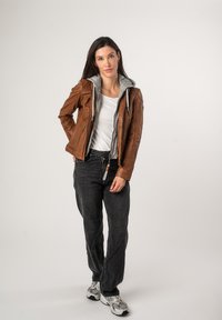 Bruine leren jas gelaagd over een grijze hoodie, met een slim fit ontwerp, rits aan de voorkant en contrasterende texturen. Draagt met een zwarte jeans en sneakers.