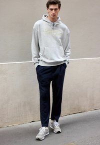 Gray hoodie with "BOULEVARD HAUSSMANN" text, large front pocket, navy trousers, and gray sneakers with white accents and laces.