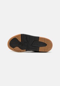 Semelle de sneaker noire avec des motifs en caoutchouc texturé. Points forts incluant une section en caoutchouc gomme et un détail de logo bien en vue. Design de crampons aigus.
