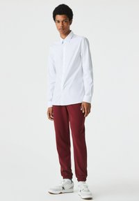 Cămașă albă cu mâneci lungi, asociată cu pantaloni sport vișinii. Tenisi albi cu accente gri. Design simplu și elegant.