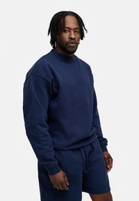 Dunkelblaues Sweatshirt mit rundem Hals und langen Ärmeln, mit einem lockeren Schnitt. Kombiniert mit passenden Shorts, die aus einem weichen Stoff bestehen.