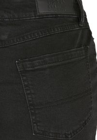 Gesäßtasche einer schwarzen Denim-Jeans mit sichtbaren Nähten und einem schwarzen Leder-Brandlabel mit der Aufschrift „Urban Classic Denim Factory.“