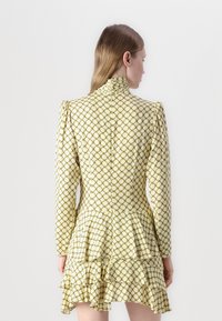 Rochie galbenă cu model, cu mâneci lungi, guler înalt și volane pe tiv. Prezintă desene geometrice într-un model în grilă.