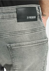 Harmaa farkut, joissa on musta nahkalaatta, jossa lukee "2Y PREMIUM" vyötäröllä. Sisältää perinteiset taskut ja ompeluyksityiskohdat.