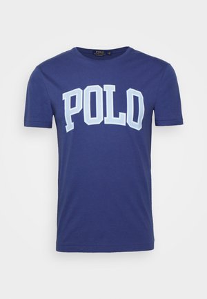 Granatowy t-shirt z krótkim rękawem i okrągłym dekoltem z dużym jasnoniebieskim i białym napisem „POLO” na środku klatki piersiowej.