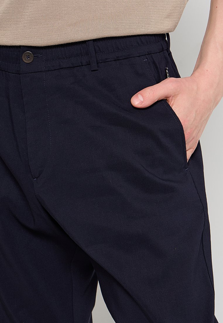 Ciemnoniebieskie, lekkie spodnie o gładkiej fakturze, z guzikami, elastycznym paskiem w talii i detalami bocznych kieszeni.