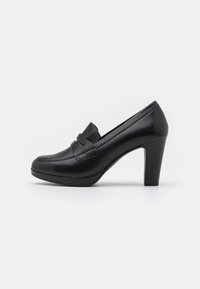 Mocassino nero in pelle con tacco alto e punta arrotondata, cuciture visibili e una cinghia decorativa sulla parte anteriore. Superficie liscia e suola imbottita.