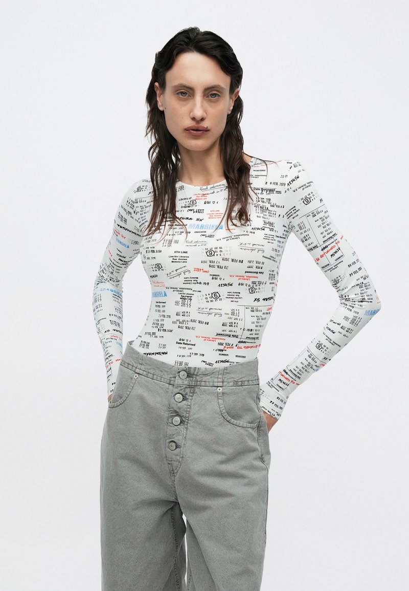 Langärmeliges Oberteil in Weiß mit gemischtem Textdruck. Graue, hochtaillierte Hose mit fünf Knöpfen und Seitentaschen. Glatte Textur, figurbetontes Design.