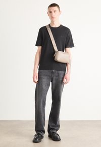 Zwarte ronde hals t-shirt, donkergrijze jeans en zwarte schoenen. Lichtbeige schoudertas met ritssluiting. Zachte structuur en minimalistisch ontwerp.