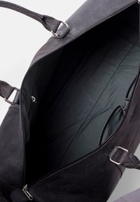 Schwarze Leder-Duffle-Tasche mit silbernen Beschlägen, Reißverschlussöffnung, Innenfach und einem weichen, dunkelgrünen Stofffutter. Verstellbare Träger.