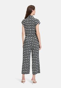 Niebiesko-kremowy kombinezon w wzory z krótkimi rękawami i wysokim kołnierzem; szerokie nogawki, luźny fason i gładka faktura.