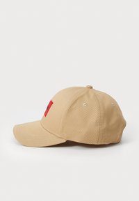 Casquette de baseball kaki avec une visière incurvée, ornée d'un patch carré rouge à l'avant et d'œillets en métal pour la ventilation.