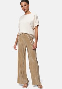 Top crème à manches courtes associé à un pantalon large doré plissé et brillant. Tissu doux et coupe décontractée, complété par des sandales à lanières.