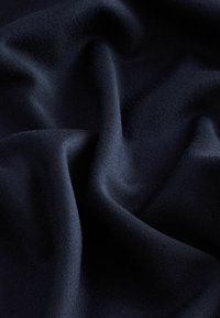 Tumši zila auduma texture ir gluda, ar mīkstām krītošām līnijām un smalkiem adījumiem, parādot bagātu dziļumu un smalku spīdumu.