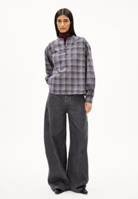 Karobluse aus Baumwolle in Blau- und Grautönen, mit einem Mandarin-Kragen und Knopfverschluss. Kombiniert mit weit geschnittenen, dunkelblauen Jeans.
