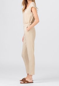 Beige top s krátkým rukávem, zkombinovaný s kalhotami světle béžové barvy s vysokým pasem. Celý vzhled doplňují hnědé sandály na klínku s designem uzlového pásku.