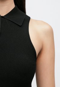 Crni rebrasti top bez rukava s ovratnikom, istaknuti kroj i glatka tekstura. Tkanina je rastezljiva i prozračna.