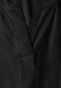 Haut en tissu noir avec un design à col en V, des coutures texturées et une finition propre et épurée. Aucun motif visible ni détails de matériel.
