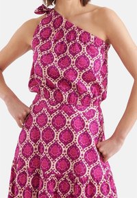 Sukienka na jedno ramię z lekkiego materiału, ozdobiona fioletowo-kremowym wzorem kwiatowym, z marszczoną talią i dekoracyjnym wiązaniem.