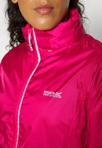 Femme portant une veste imperméable Regatta Great Outdoors rose vif avec un col montant zippé et une bande réfléchissante.