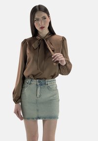 Brun satinbluse med bundet halsudskæring, pufærmer, kombineret med en højtaljet lys denim mininederdel med falmet vask og forlommer.