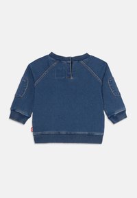 Bakre vy av en blå denimtröja för småbarn med ribbade manschetter, nederkant, krage, lappar på ärmarna och en kort dragkedja på ryggen.