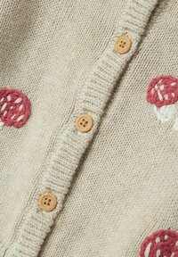 Strickjacke in Beige mit strukturiertem Stoff, ausgestattet mit runden Holzknöpfen und buntem Stickerei-Muster von Pilzen in Rot und Weiß.