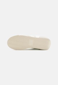 Suela de sneaker blanca con un patrón de espiga texturizado. Punta redondeada, diseño plano, hecho de goma. Marca minimalista visible.