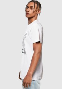 White cotton t-shirt with short sleeves, featuring a black graphic of a hand and wings. The design has fine lines and detailed accents.